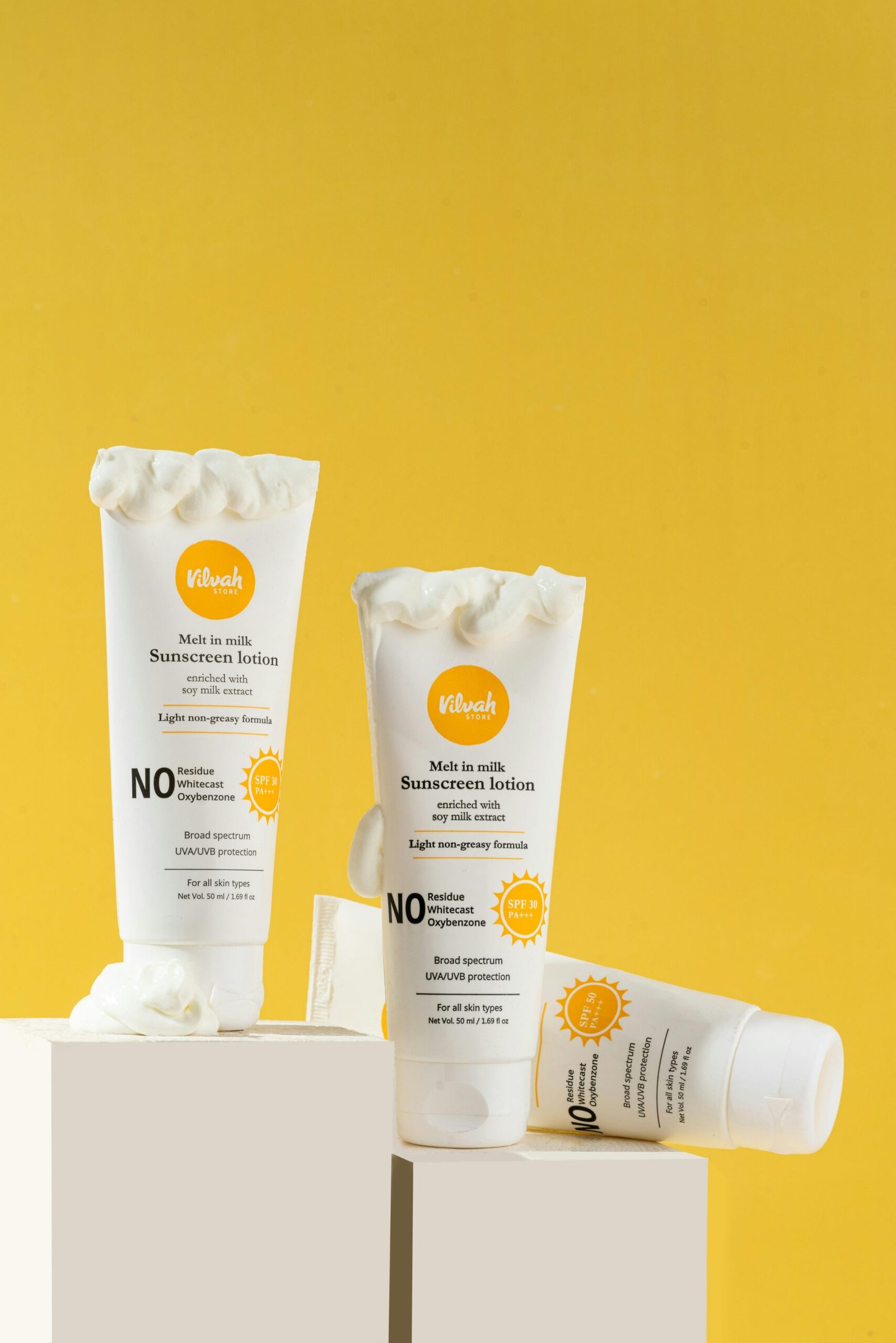 Close-up of sunscreen tubes displayed on white blocks against a yellow background, ideal for skincare promotions.